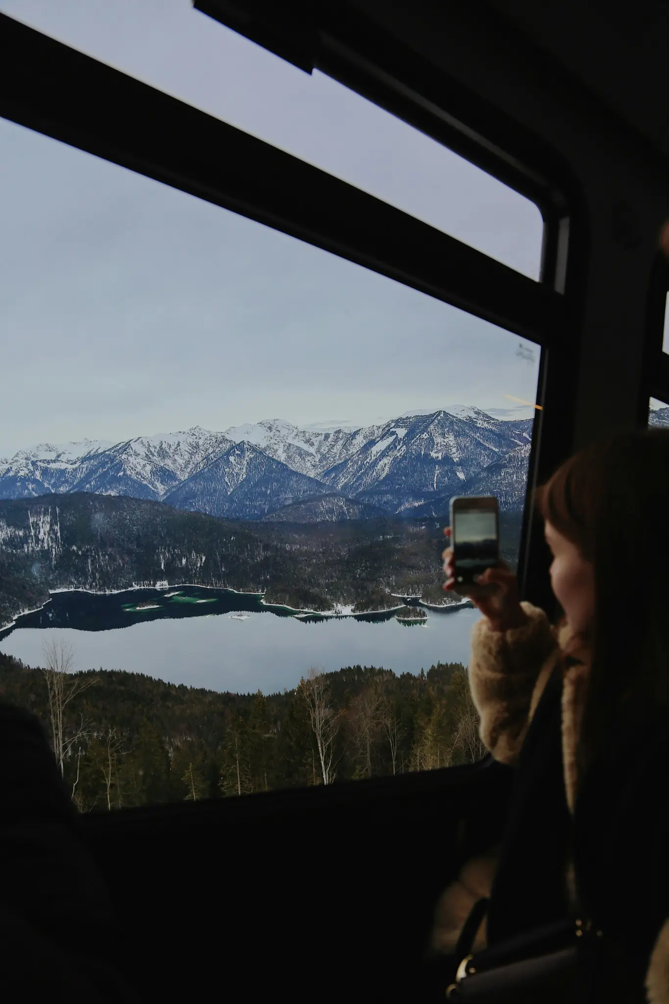 Una viajera fotografía un lago y montañas nevadas desde la ventanilla