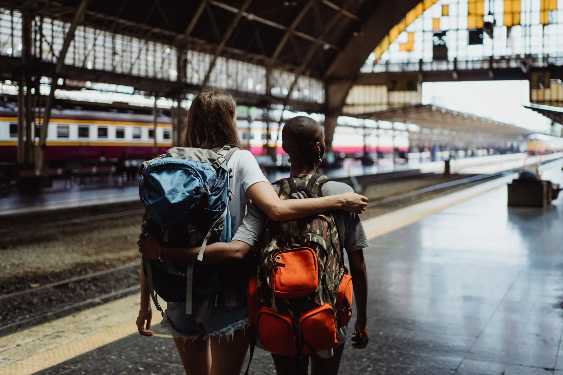 Dos personas viajeras abrazadas en un andén con sus mochilas