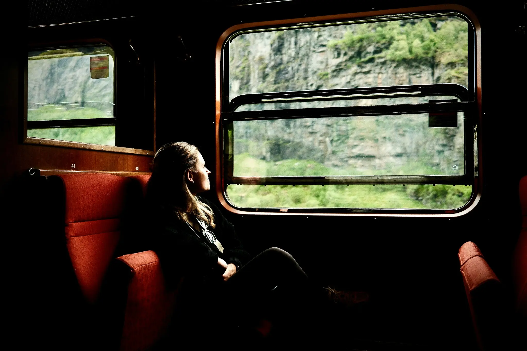 Una viajera observa el paisaje desde un coche de tren de tonos rojos