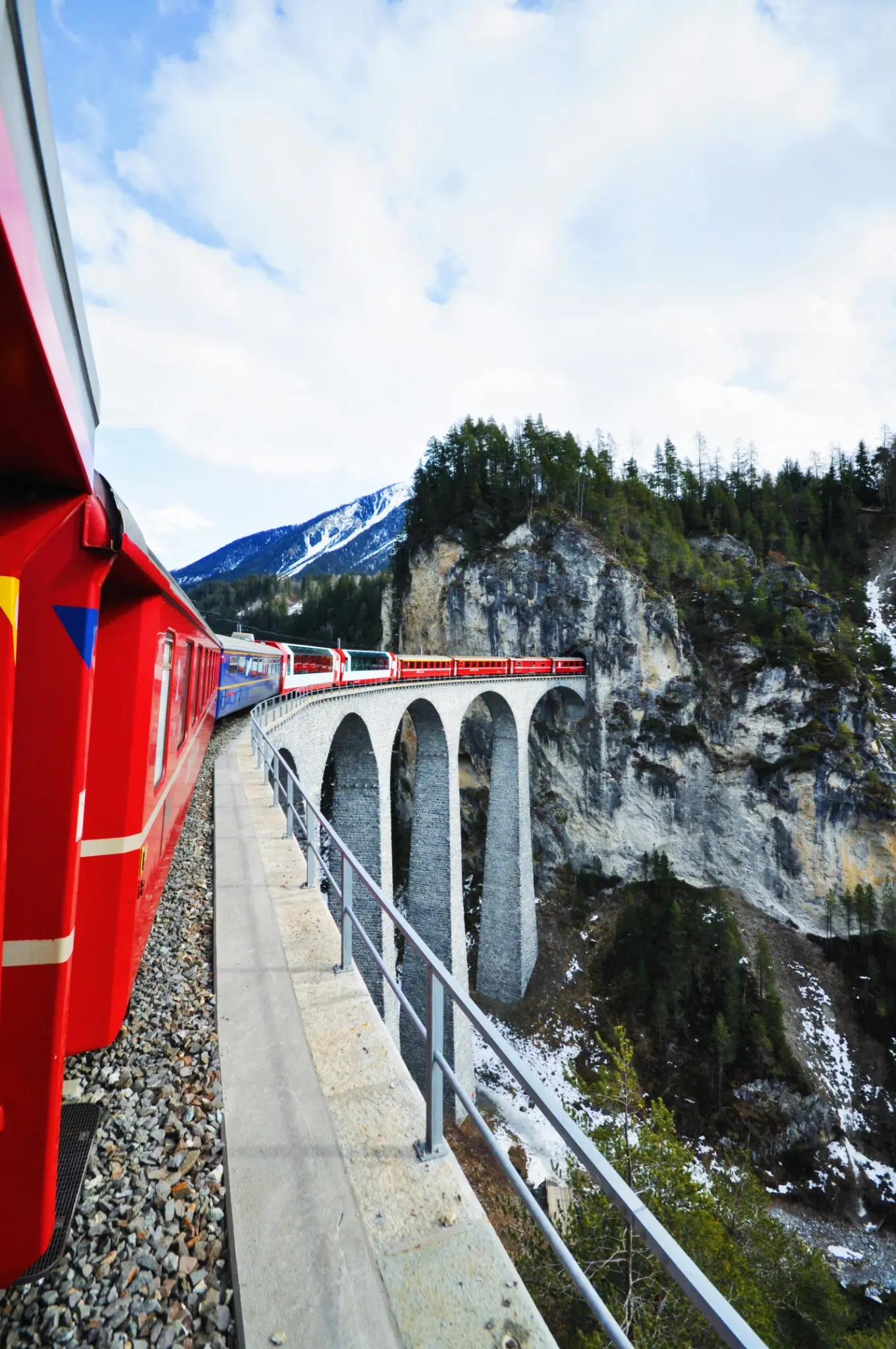 Vista desde un tren rojo al cruzar un viaducto de piedra entre paredes de roca