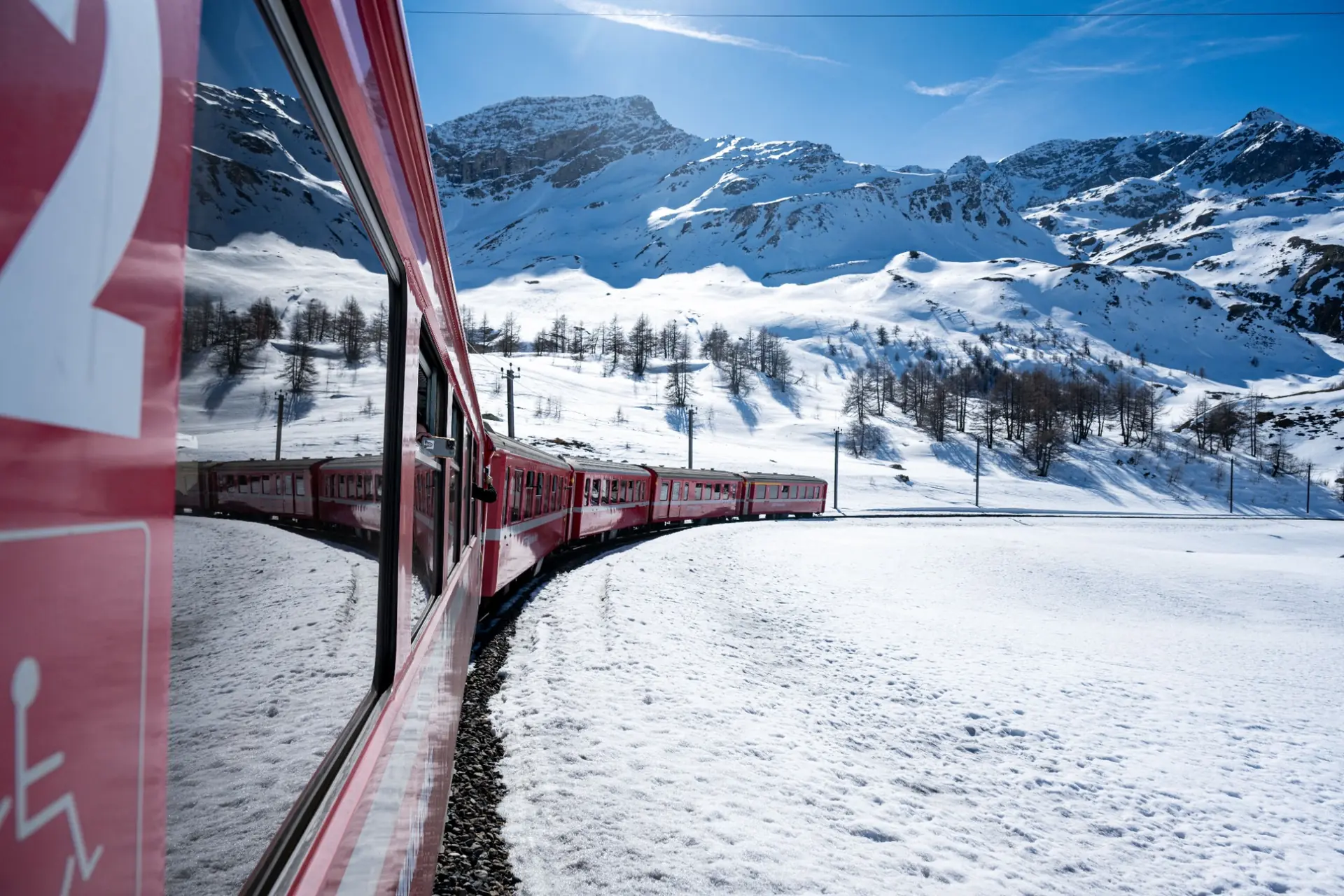 Tren rojo avanzando en curva frente a un paisaje alpino cubierto de nieve